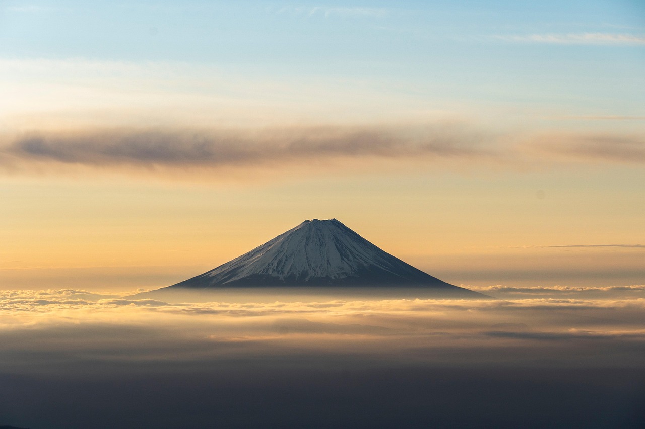 Mount Fuji rising above clouds during sunrise with a soft golden sky