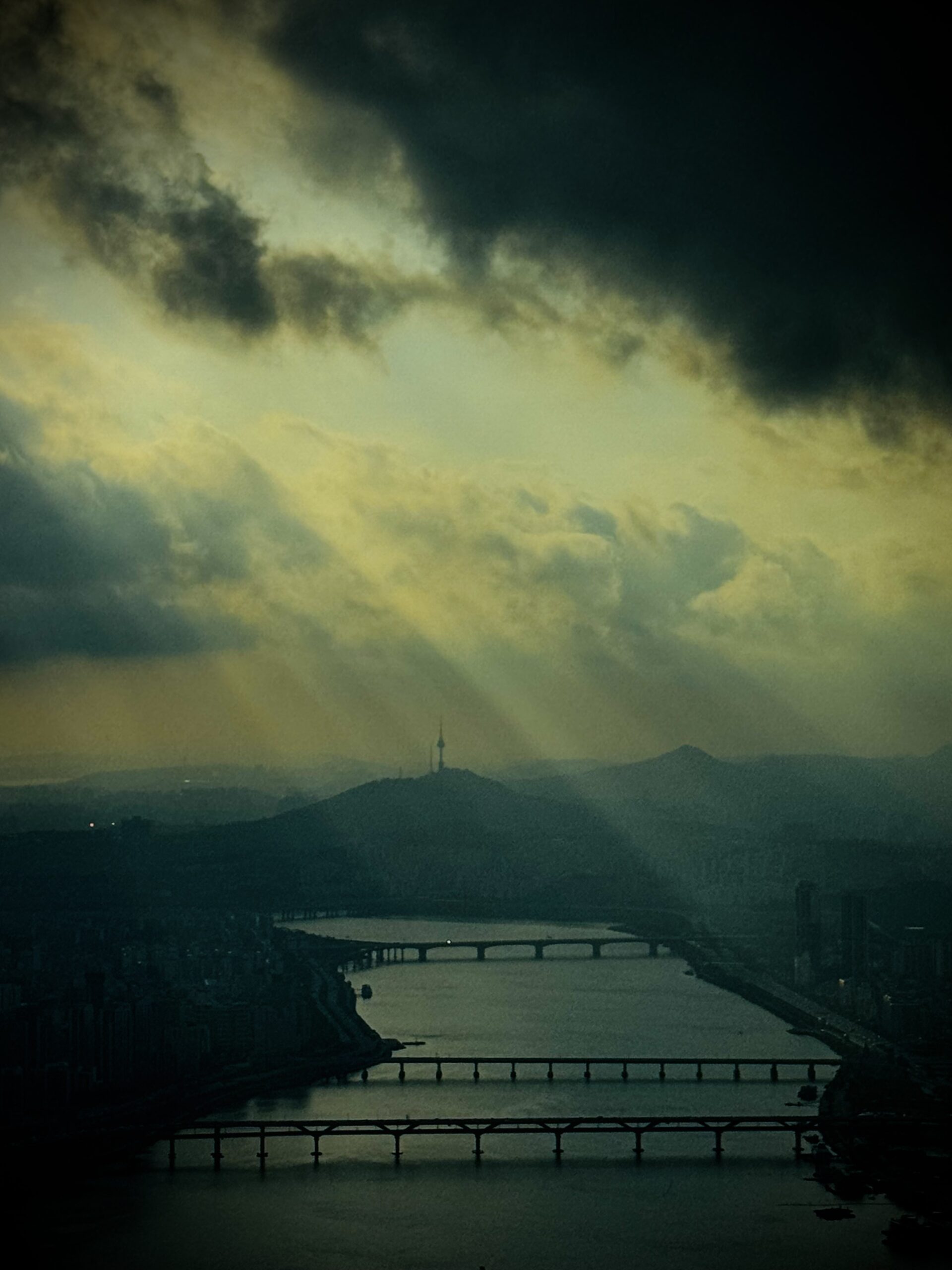 Sunbeams breaking through dark clouds over the Han River and Seoul skyline with N Seoul Tower in the distance