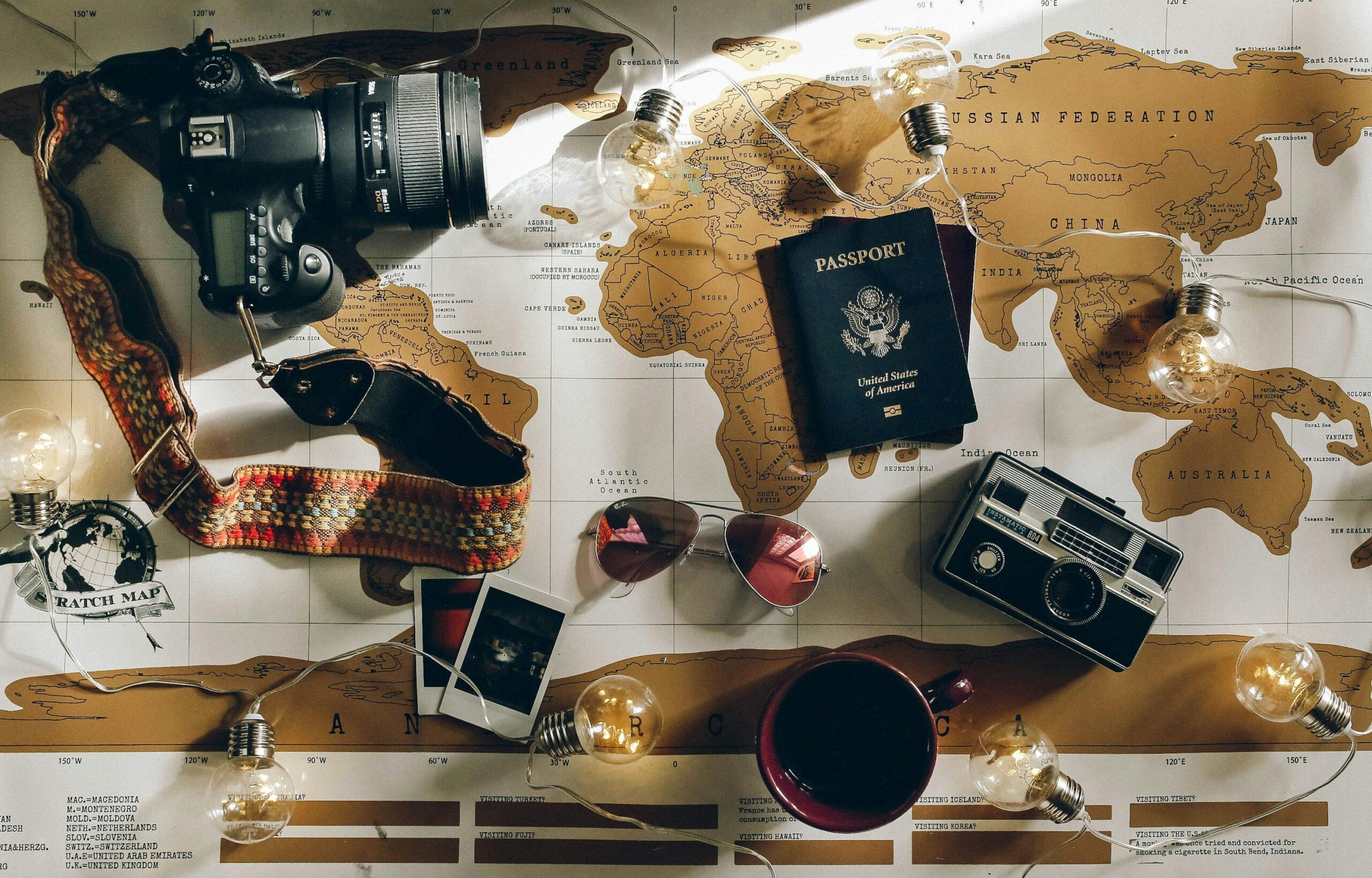 Travel flat lay with camera, passport, world map, sunglasses, coffee cup, and vintage radio