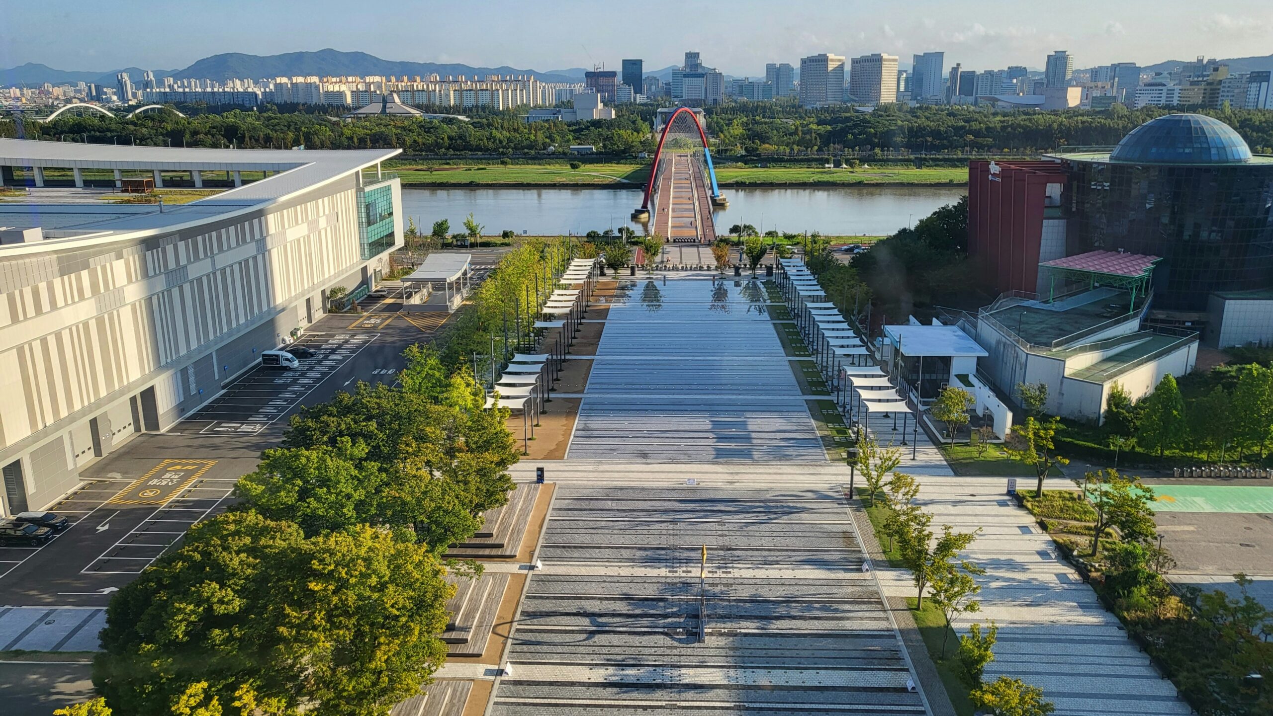 Daejeon city view with a wide public plaza, modern buildings, greenery, and a bridge across the river.