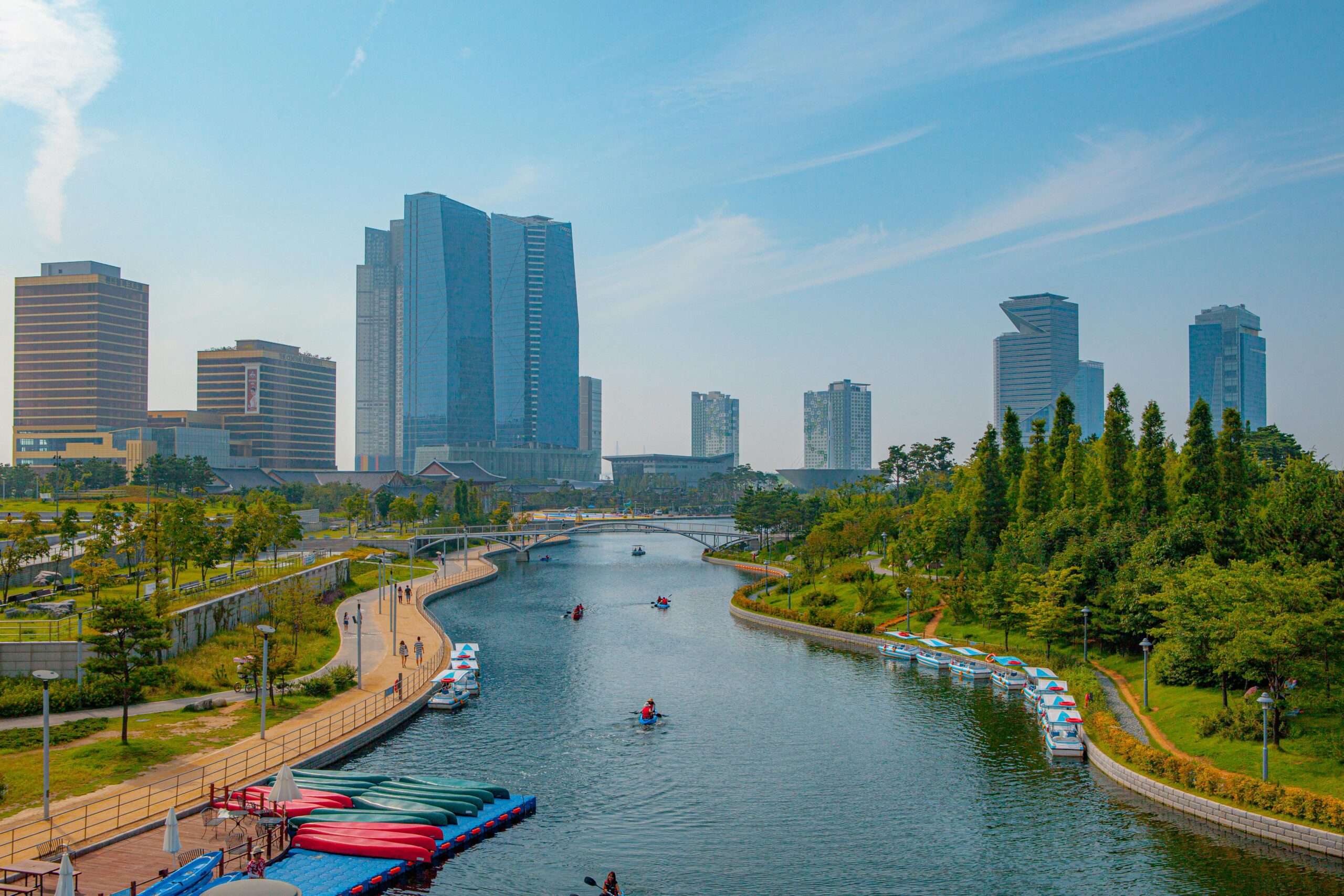 Songdo Central Park in Incheon with a canal, boats, walking paths, trees, and modern high-rise buildings.