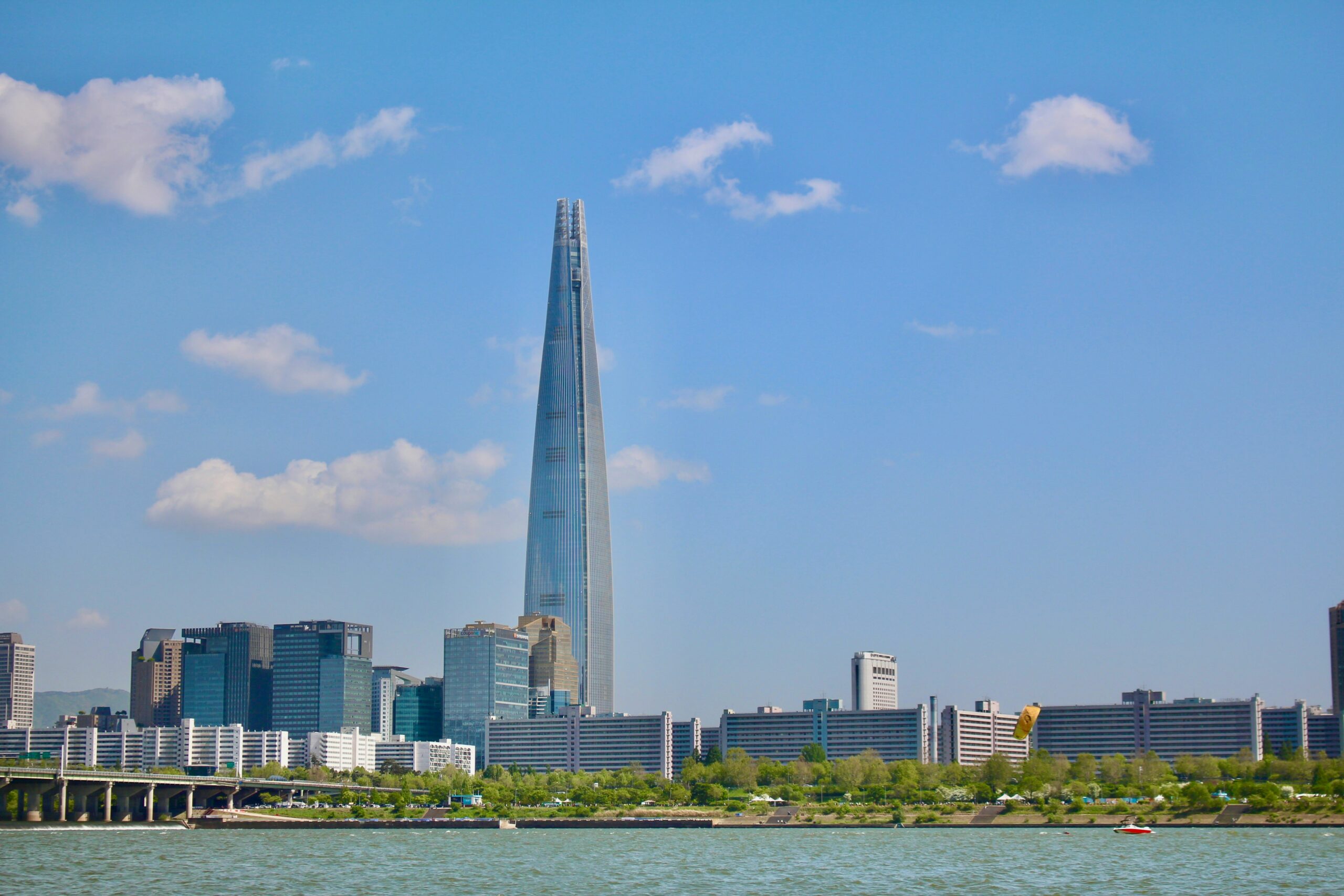 Lotte World Tower in Seoul rising above the Han River under a clear blue sky.